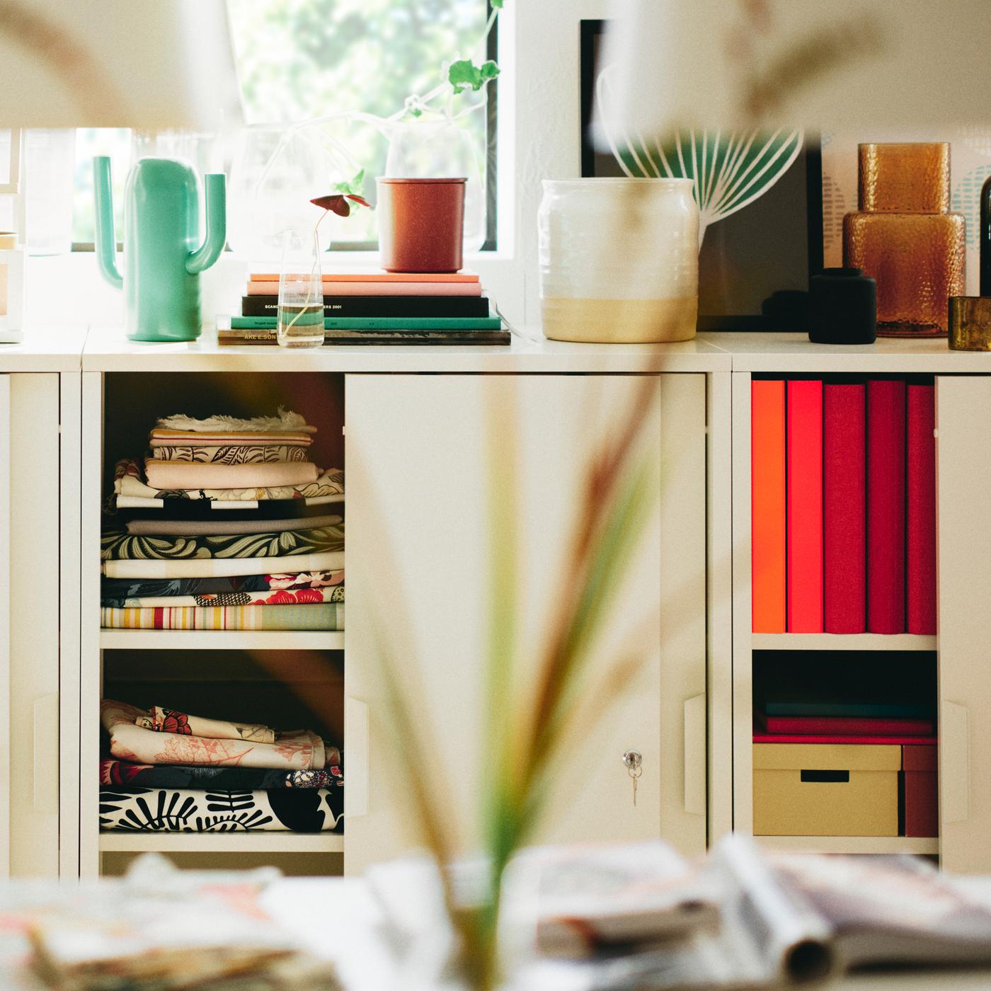 Two white TROTTEN cabinets with sliding doors with a bright green ÄRTBUSKE vase/watering can on top of one of them.