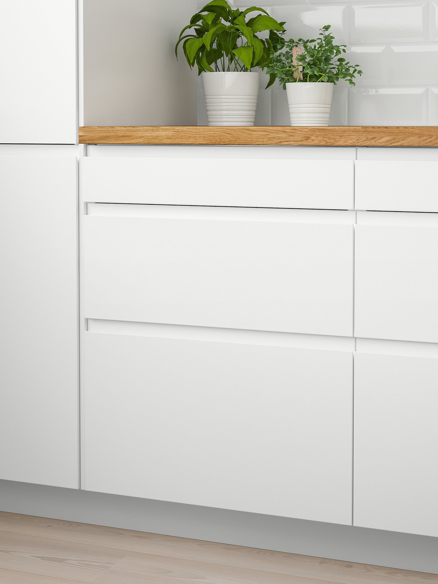 Two white wall cabinets with doors and a wooden worktop on which there are two green plants. Below there are six white drawers.