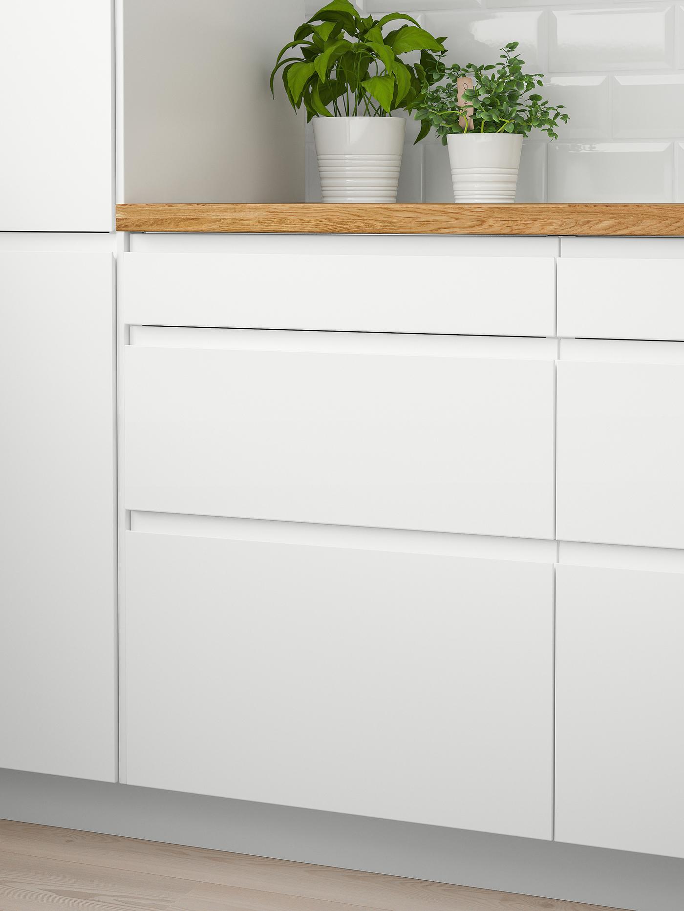 Two white wall cabinets with doors and a wooden worktop with two green plants on top and six white drawers below.