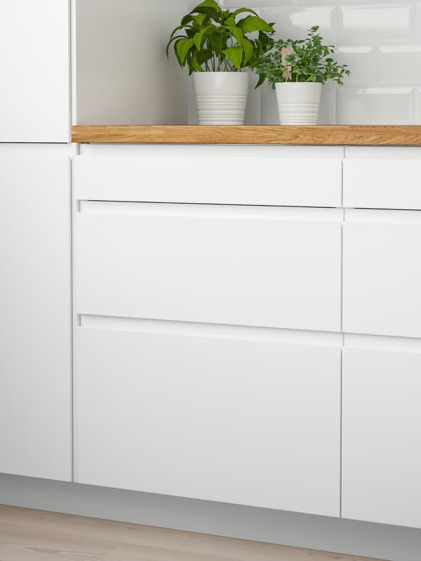 Two white wall cabinets with doors and a wooden worktop with two green plants on top and six white drawers below.