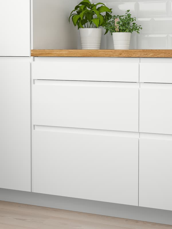 Two white wall cabinets with doors and a wooden worktop with two green plants on top and six white drawers below.