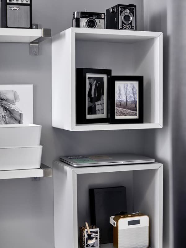 Two, white, wall-mounted storage cabinets with framed photographs, vintage cameras and other items.