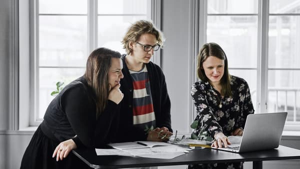 Two women and a man standing at a standing desk looking at something on a laptop computer