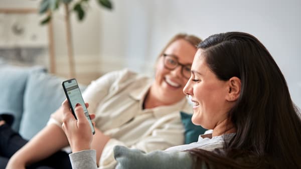 Two women are looking at their mobile phones and laughing