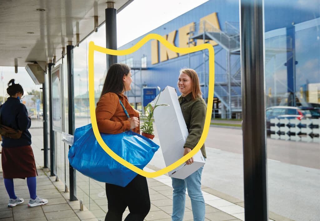Two women are standing with their IKEA purchases in front of an IKEA store and chatting
