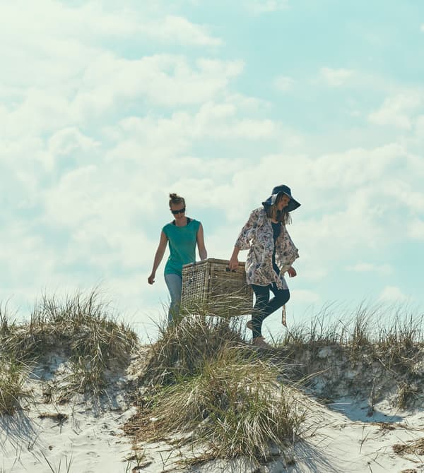 Two women carry a large wicker basket to the beach.