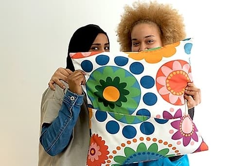 Two women holding a patterned cushion from the ÅTERSTÄLLA collection