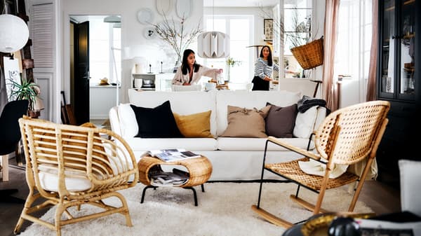Two women in a white country-style living area with a white BACKSÄLEN sofa in front of a rug and two rattan armchairs.