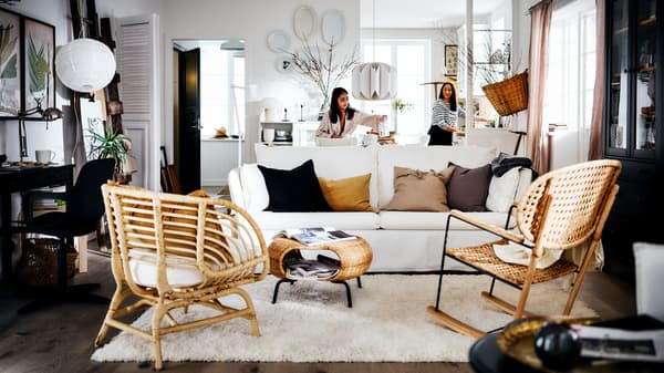 Two women in a white country-style living area with a white BACKSÄLEN sofa in front of a rug and two rattan armchairs.
