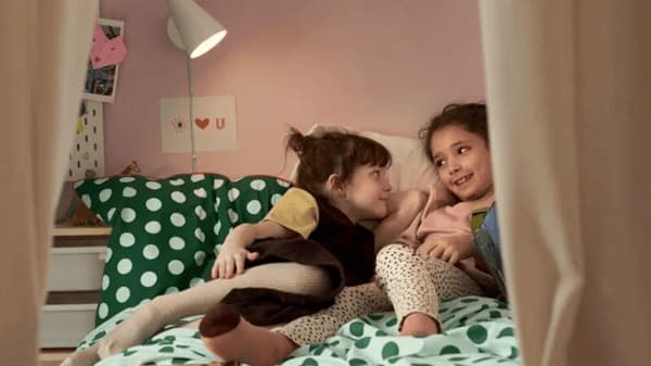 Two young girls are lying on a cozy bed with green polka dot bedding, smiling and enjoying a warm moment together in a softly lit, child-friendly room.
