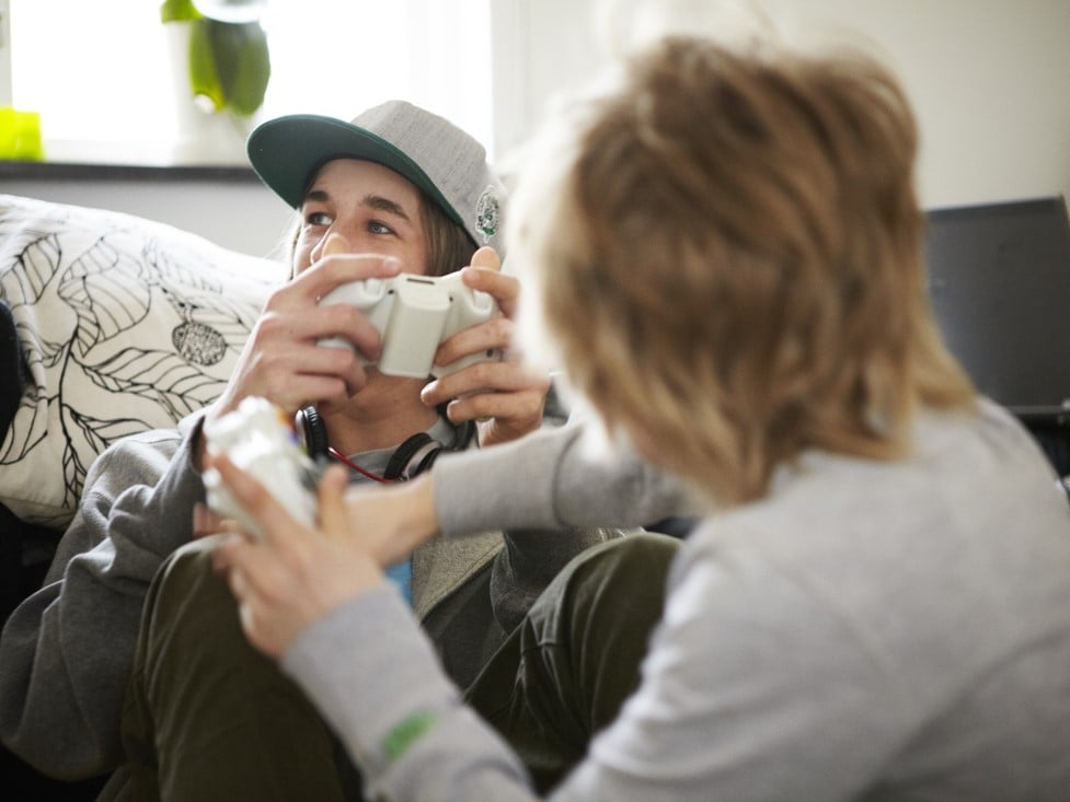 Two young people sitting casually on the floor, playing video games, with a controller in their hand