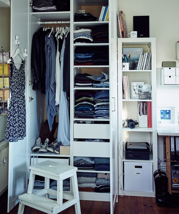 Ubrania ułożone na półkach i zawieszone na drążku w szafie Stine.