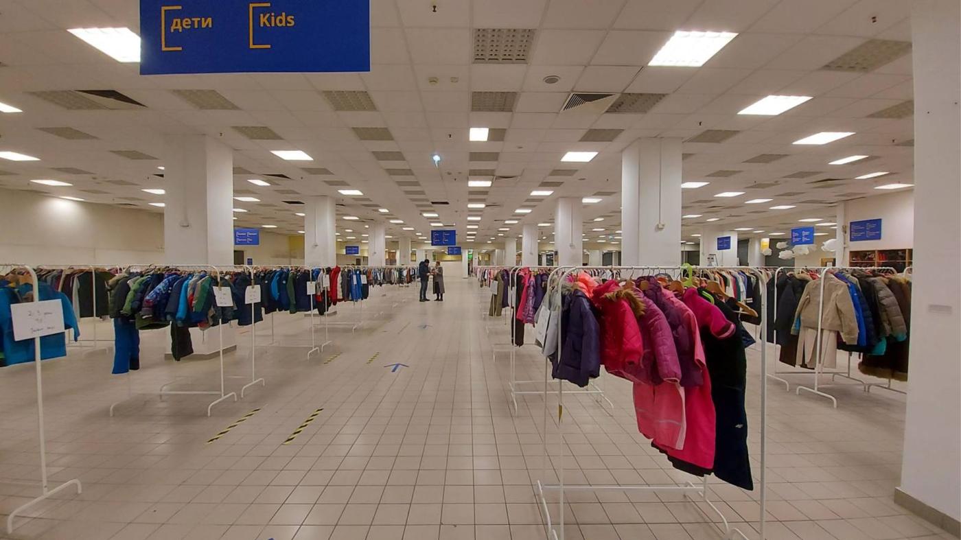 Ubrania wiszące na wieszakach IKEA, ustawione w rzędach na dużej hali w dawnej galerii handlowej