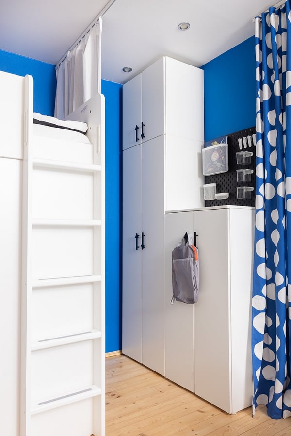 Учебная зона для детей с белым столом, синими шторами в горошек, дневным светом и жёлтой тележкой для хранения