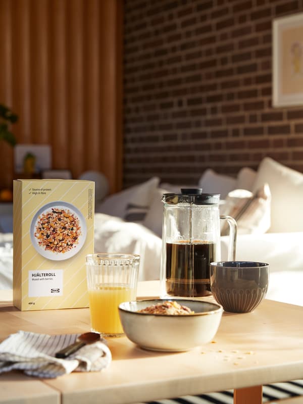 Ukusan doručak na stolu u dnevnoj sobi, uključujući čašu sa sokom, vrč s kavom i HJÄLTEROLL muesli.