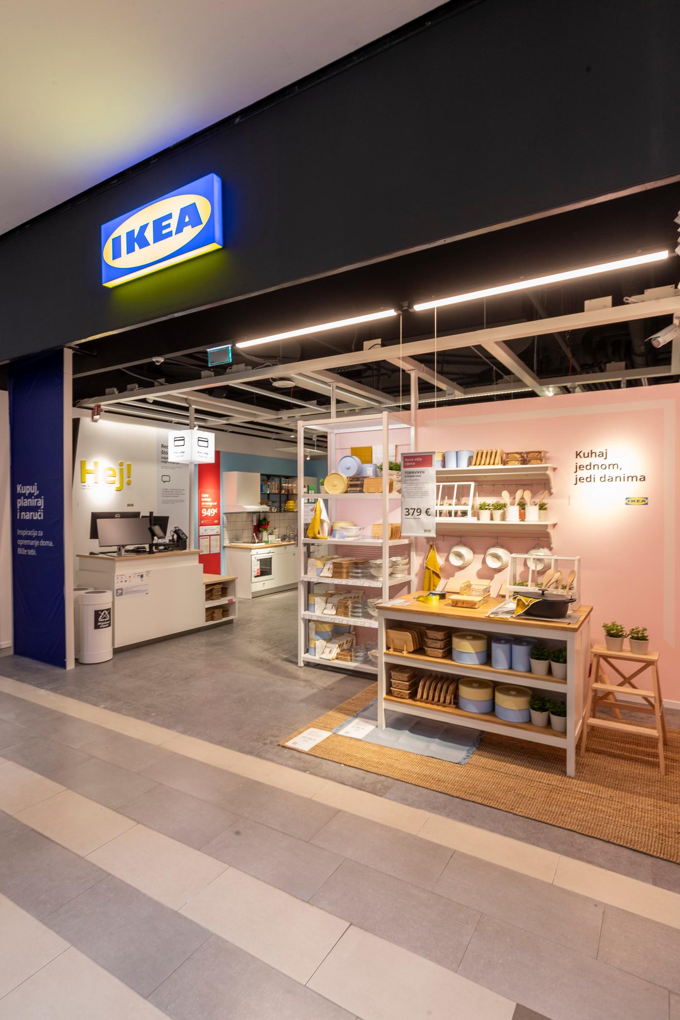Ulaz u IKEA studio za planiranje u tržnom centru s osvijetljenim logotipom, izložbenim policama s kuhinjskim priborom i ružičastim zidom s natpisom "Kuhaj jednom, jedi danima".