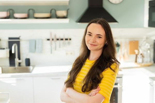 Улыбающаяся женщина в современной кухне с белыми шкафами и пастельно-голубой стеной