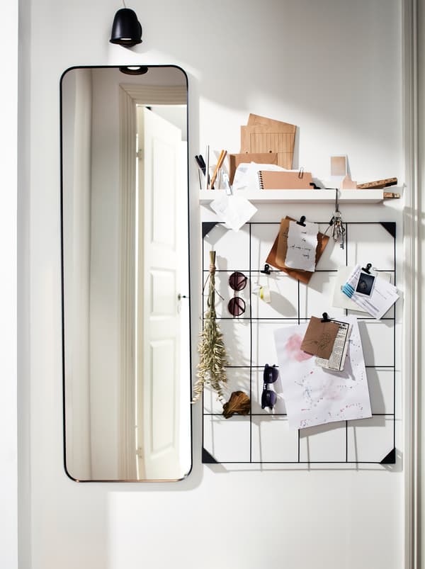 Um espelho LINDBYN alto, um quadro para mensagens SÖSDALA em aço preto com molas e uma prateleira, com notas e óculos de sol.
