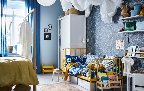 Um quarto com um esquema de cores em azul e amarelo, com uma cama de adulto num lado e a cama de criança no outro lado.