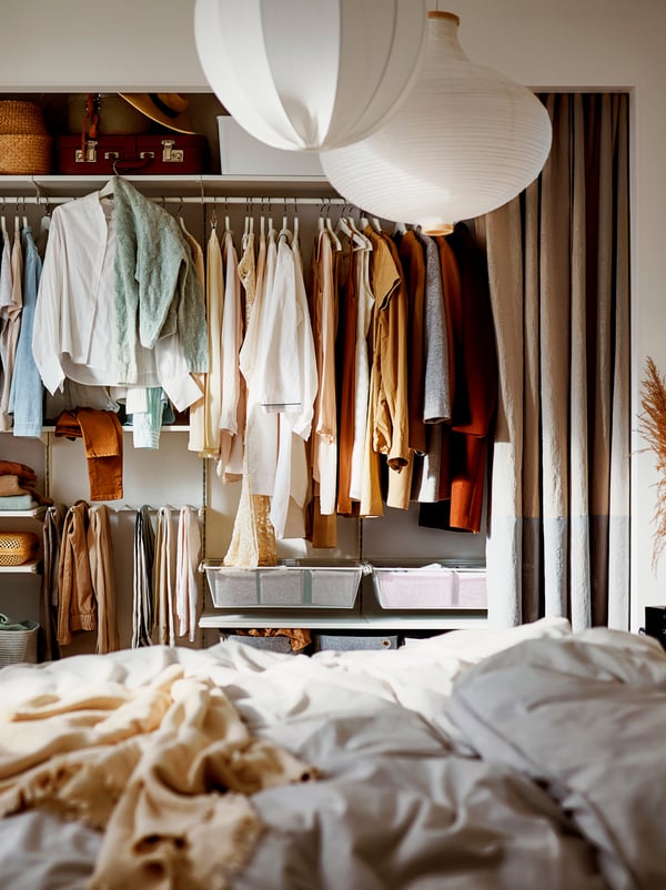 Um roupeiro com cortinados como “portas” e uma combinação de cabides e prateleiras para malas de viagem e caixas para os artigos mais pequenos.