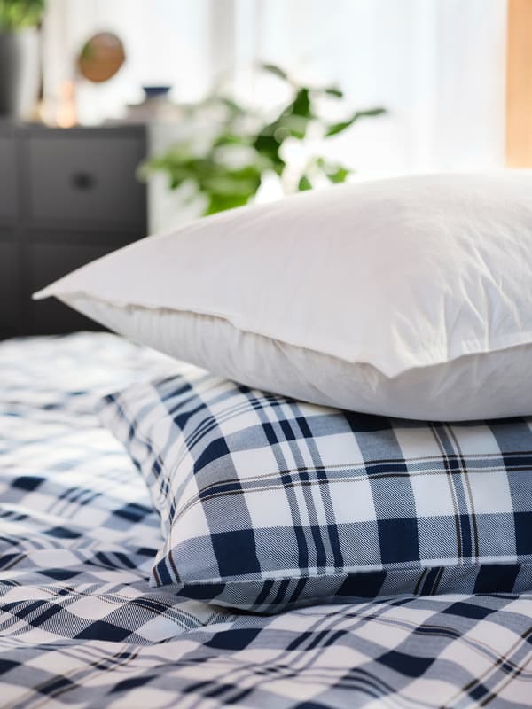 Uma almofada LUNDTRAV alta está em cima de outra almofada coberta com uma fronha aos quadrados e um edredão aos quadrados.