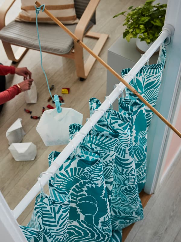 Uma cortina de duche GATKAMOMILL colocada numa entrada. Uma cana de pesca de brincar, que está a ser segurada por cima, tem um saco de doces preso à linha.