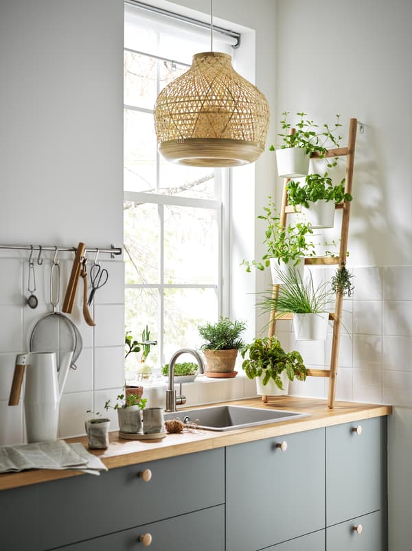 Uma cozinha com uma floreira SATSUMAS em bambu, em forma de escada, com cinco vasos, em cima de uma bancada à frente de uma janela.