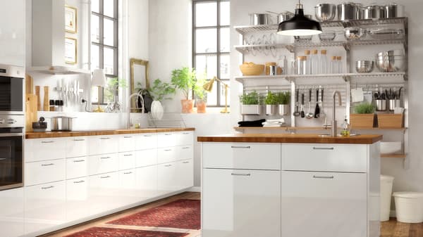 Uma cozinha grande, em branco, com uma ilha e portas em branco brilhante, uma bancada em carvalho e uma estante na parede.