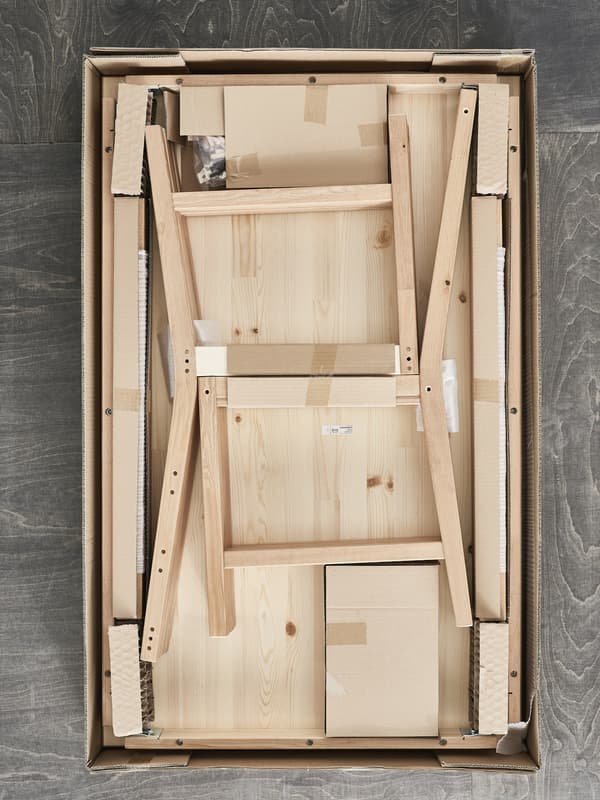 Uma embalagem plana da IKEA aberta a mostrar uma cadeira de pinho pronta para ser montada.