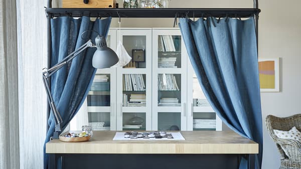 Uma ilha de cozinha numa sala com a estrutura superior a ser utilizada como espaço de arrumação e varão para cortinados em azul.