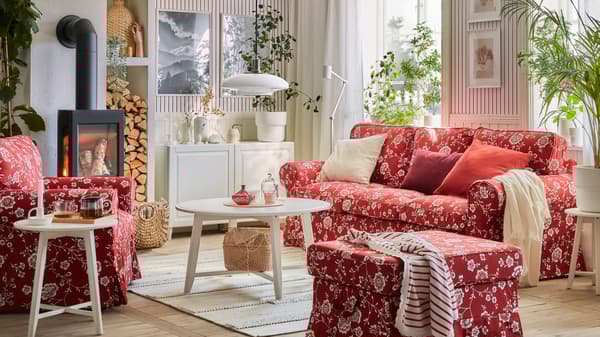 Uma sala com um sofá EKTORP, uma poltrona e um repousa-pés num padrão florido em vermelho/branco, mesas redondas e um aparador.