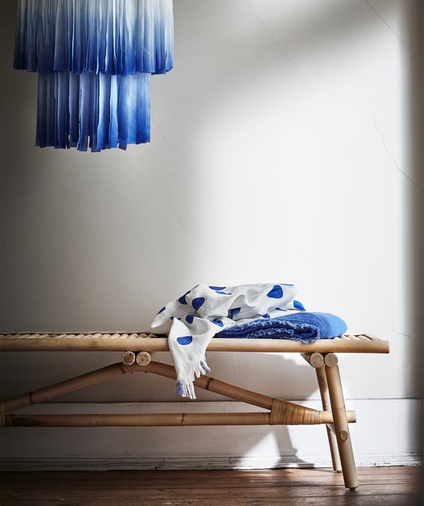 Un abat-jour en tissu bleu suspendu au-dessus d’un banc en rotin.