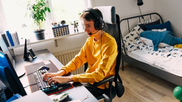 Un adolescent assis dans sa chambre sur une chaise JÄRVFJÄLLET à une table LINNMON/ALEX, portant un casque d’écoute, est en train d’utiliser un ordinateur.