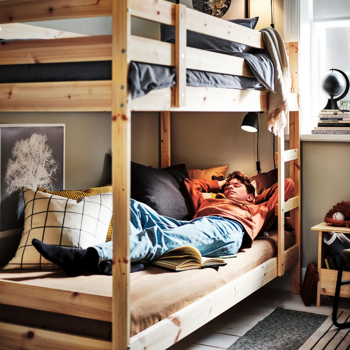 Un adolescent endormi dans une structure de lits superposés MYDAL en pin, avec le lit supérieur habillé d’une housse de couette et d’une taie KOPPARBLAD bleu foncé.