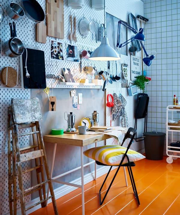 Un angolo cucina con pannelli portaoggetti e utensili da cucina appesi a dei ganci, un tavolo e sedie pieghevoli - IKEA