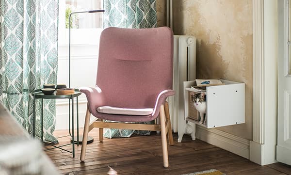 Un angolo di un soggiorno con una poltrona rosa VEDBO. Accanto, un tavolino in metallo verde VEDBO e una mensola coon un gatto che si affaccia.
