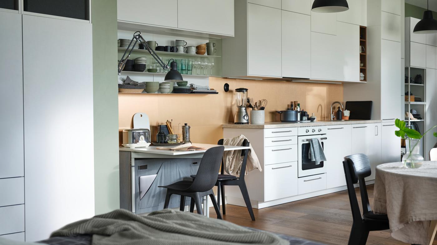 Un apartament diàfan amb una taula de fulles abatibles KALLHÄLL amb emmagatzematge i una cuina METOD blanca amb armaris des del terra fins al sostre.