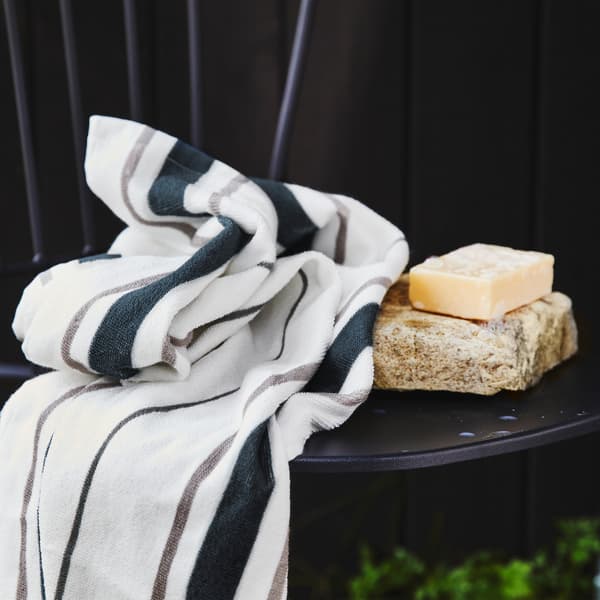 Un asciugamano a righe blu e grigie su una sedia nera con una saponetta appoggiata su una pietra.