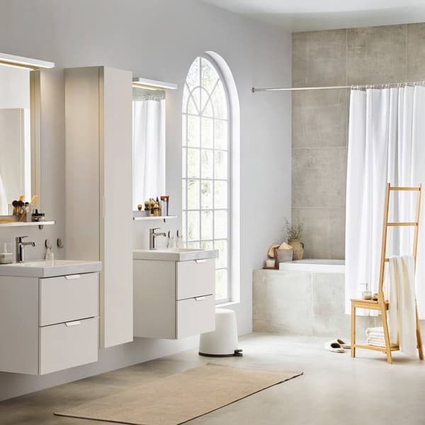 Un bagno ampio in stile moderno sui toni del bianco. Ci sono due mobili con lavabo e specchi, un'ampia finestra da cui entra luce, una vasca con tenda per doccia e una sedia portasciugamani RÅGRUND.