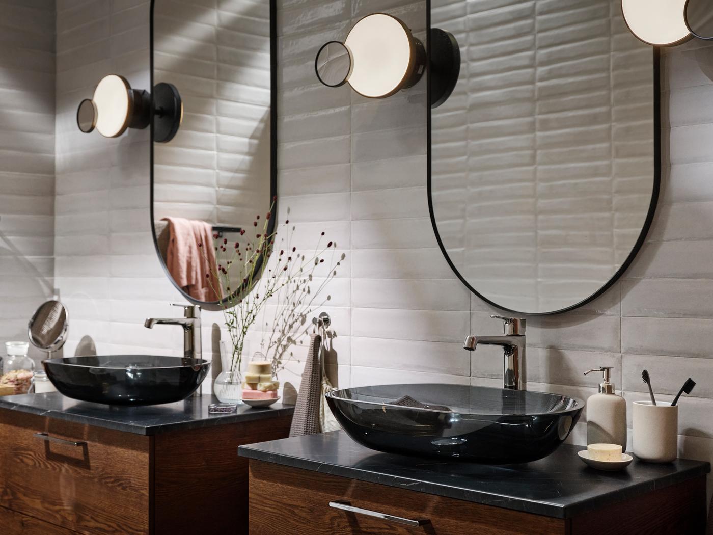 Un bagno con due lavabi da appoggio OXMYREN in vetro grigio scuro; sopra, due specchi LINDBYN neri.
