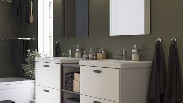 Un bagno con una combinazione di mobili bianchi, elementi a giorno, un piano di appoggio e doppio lavabo. Ai lati, biancheria appesa e una vasca da bagno con accessori.