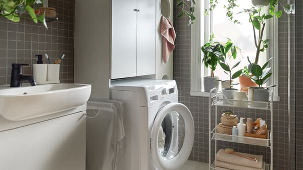 Un bagno con una lavatrice UDDARP bianca e un carrello HORNAVAN bianco con oggetti e un mobile NYSJÖN, anch'esso bianco - IKEA.