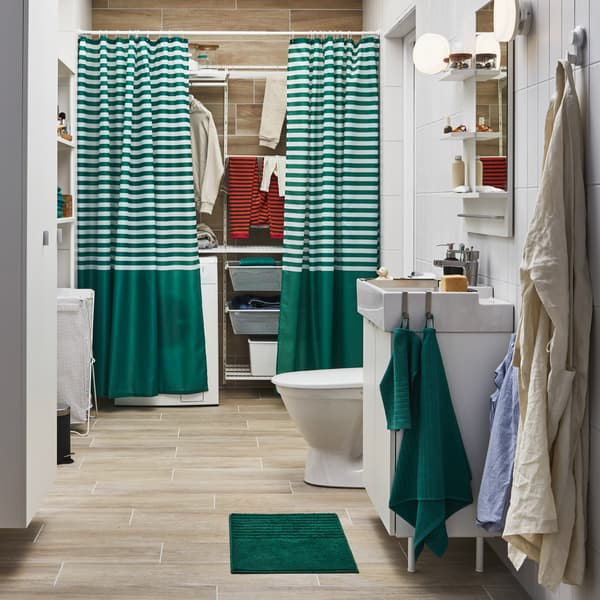 Un bagno con una zona lavanderia semi-nascosta dietro a tende per doccia a righe, un lavabo bianco e asciugamani verdi - IKEA