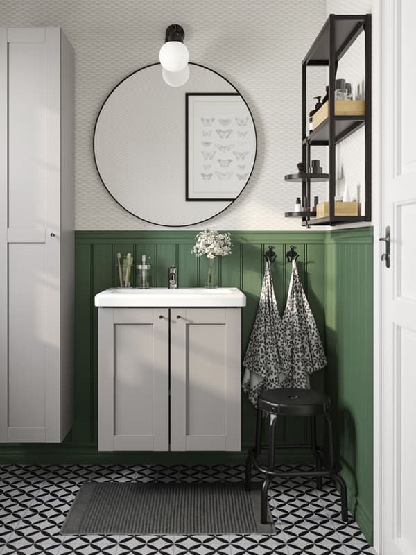 Un bagno con uno specchio tondo, un pavimento geometrico e parete verde.