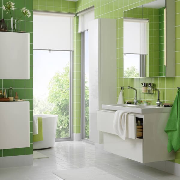 Un bagno molto ampio in stile moderno di colore bianco con doppio lavabo. Le pareti hanno piastrelle di colore verde in due diverse sfumature. C'è un'ampia porta finestra da cui entra luce.