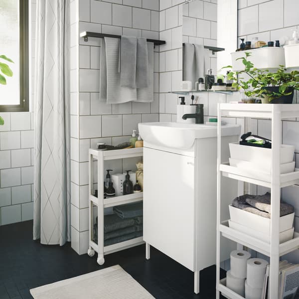 Un bagno monocromatico in stile contemporaneo, con diversi elementi contenitori salvaspazio, scatole e piante verdi da interno.