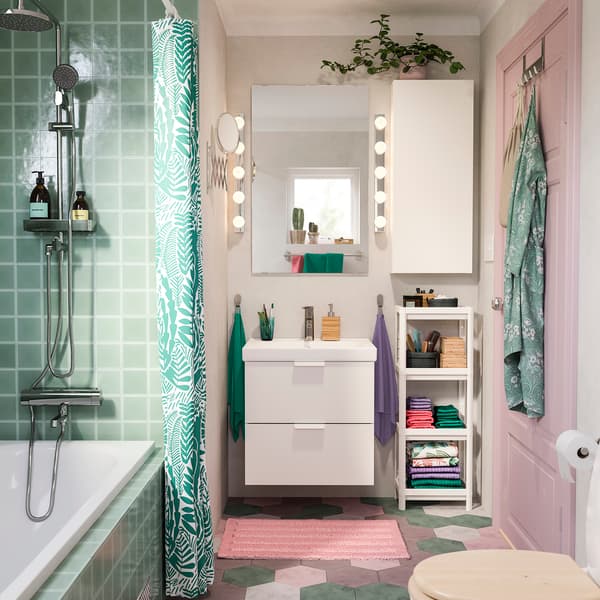 Un bagno sui toni del verde e del rosa. A sinistra, c'è una vasca con una tendina colorata. Al centro un lavabo con mobile dotato di cassetti. Ci sono indumenti appesi ad una porta e alcuni oggetti ordinati su uno scaffale bianco.