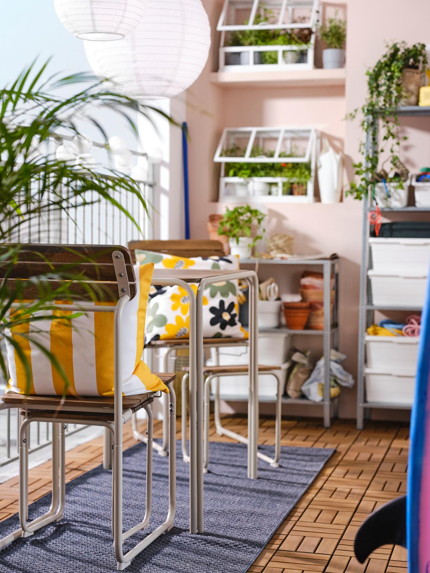 Un balcon aux murs roses avec une table à manger FURUÖN, deux chaises, deux repose-pieds, des étagères et une serre.