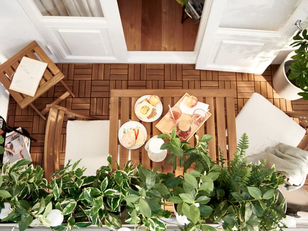 Un balcon avec des meubles NÄMMARÖ et un caillebotis RUNNEN en lattes d'acacia, et des plantes vertes artificielles FEJKA.