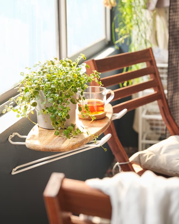 Un balcon avec une mini table d’appoint formée par une planche à découper placée sur des crochets SKRÄLL, et sur laquelle sont posées une tasse de thé et une plante. Une chaise se trouve sur le côté.